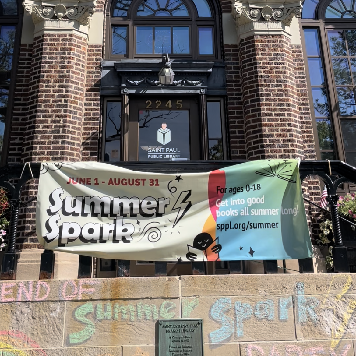 A photo of the St. Anthony Park Branch Library front entrance with their summer spark banner.